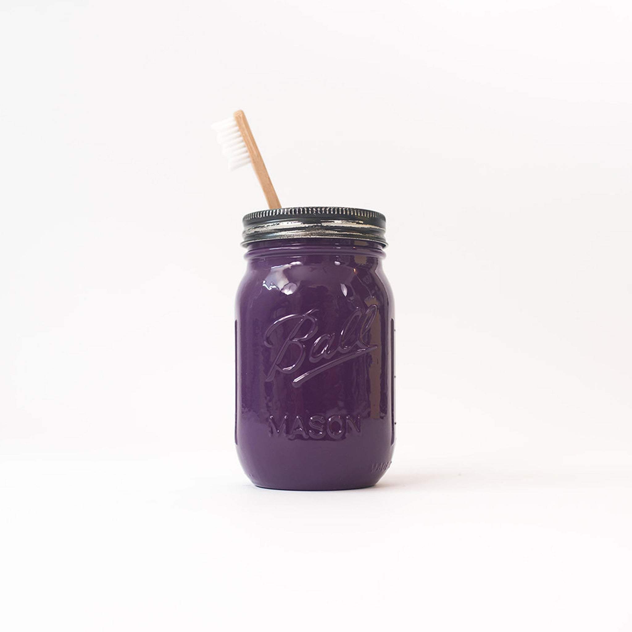 Av purple mason jar with a toothbrush in it on a white background.