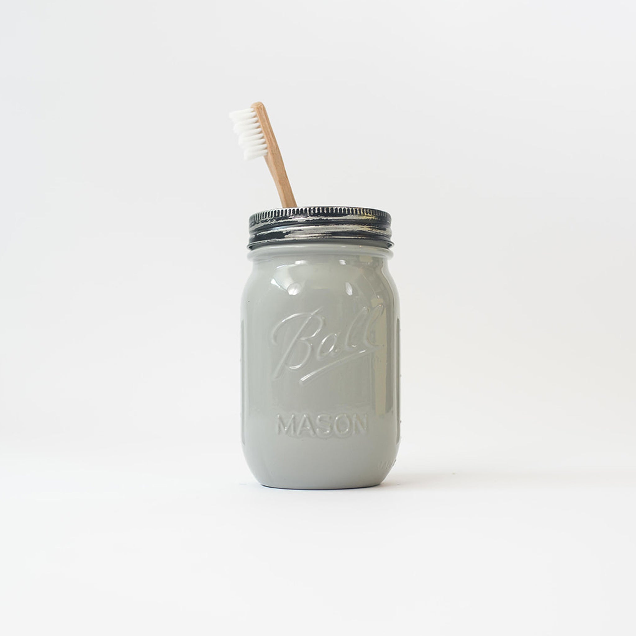 A grey mason jar with a toothbrush in it on a white background