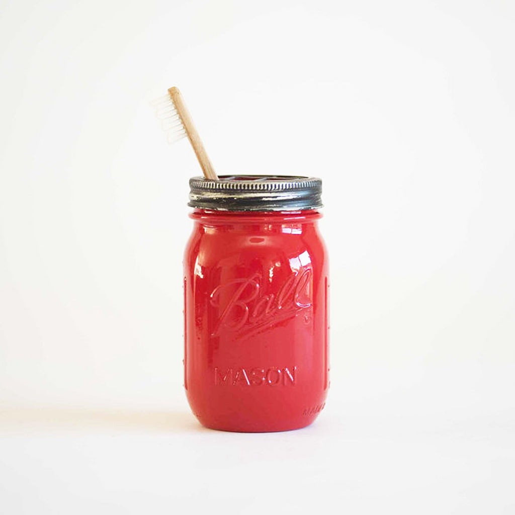 A red mason jar with a toothbrush in it on a white background
