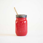 A red mason jar with a toothbrush in it on a white background