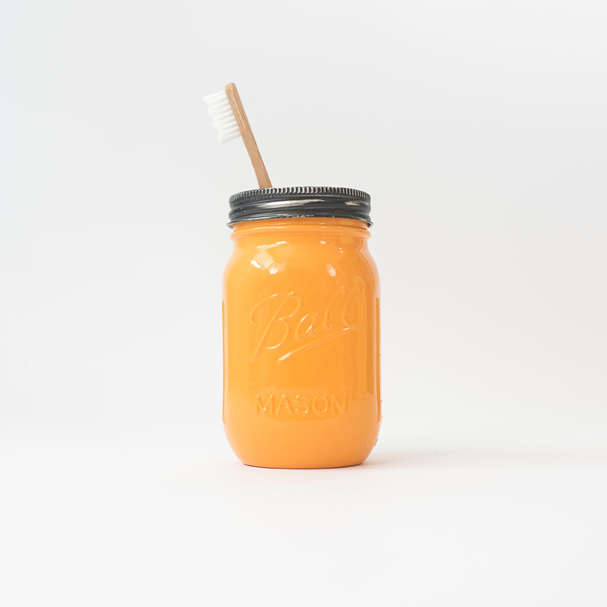 A goldenrod mason jar with a toothbrush in it on a white background