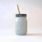 A grey mason jar with a toothbrush in it on a white background.