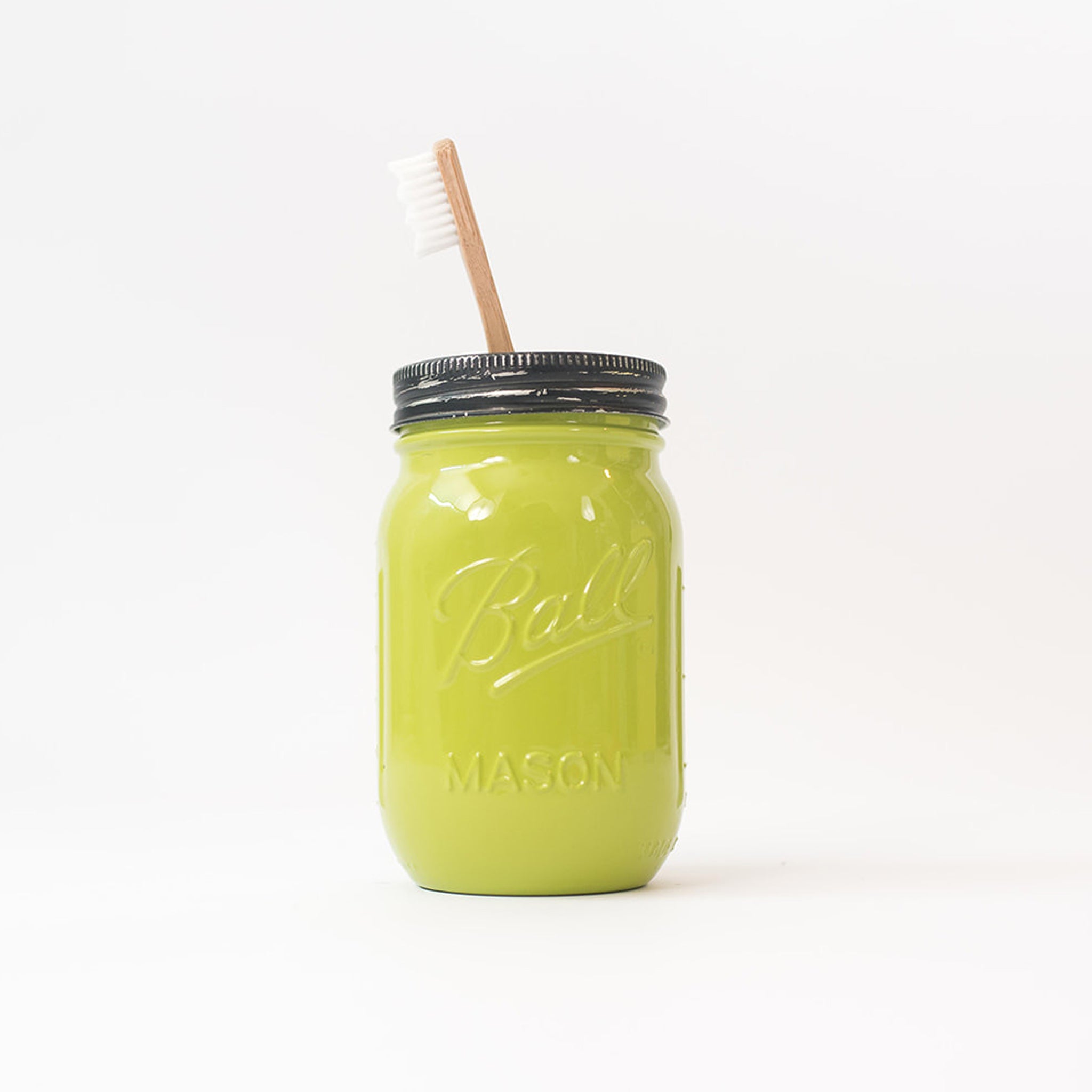 Lime green mason jar with a toothbrush in it on a white background.