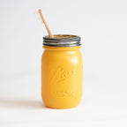 A yellow mason jar with a silver lid and wooden toothbrush on a white background.