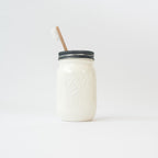 A white mason jar with wood toothbrush on a white background.