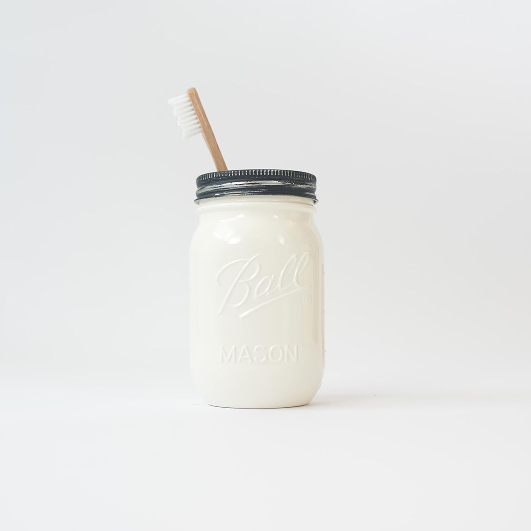 A white mason jar with wood toothbrush on a white background.