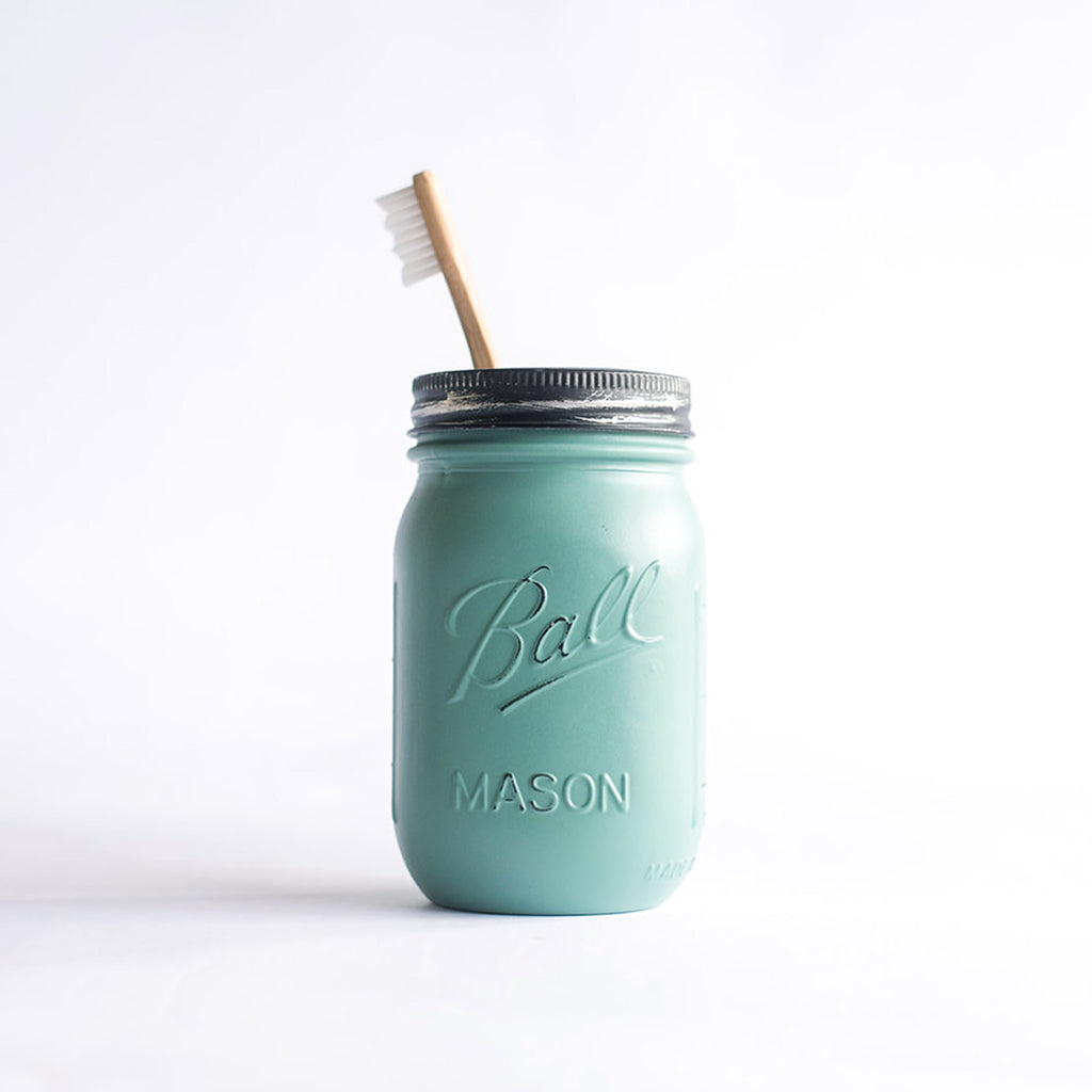 Forest green mason jar with a silver lid and wooden toothbrush on a white background.