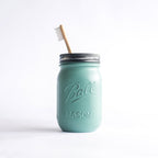 Forest green mason jar with a silver lid and wooden toothbrush on a white background.