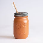 Brown mason jar with a metal lid and a wooden toothbrush on a white background.