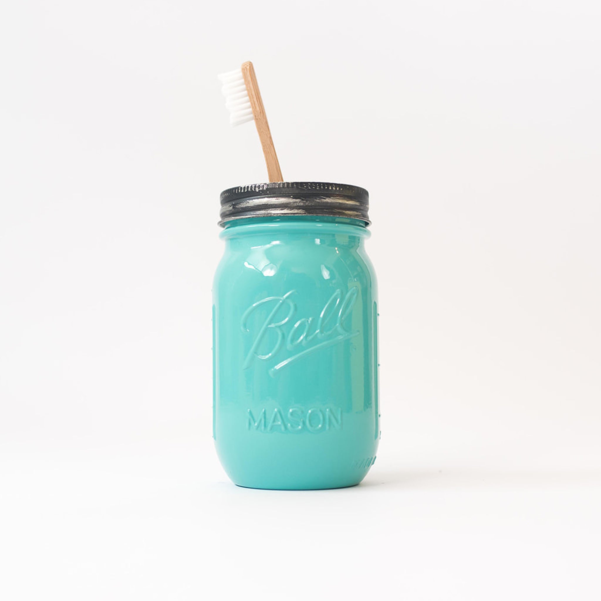 Turquoise mason jar with a toothbrush in it on a white background.