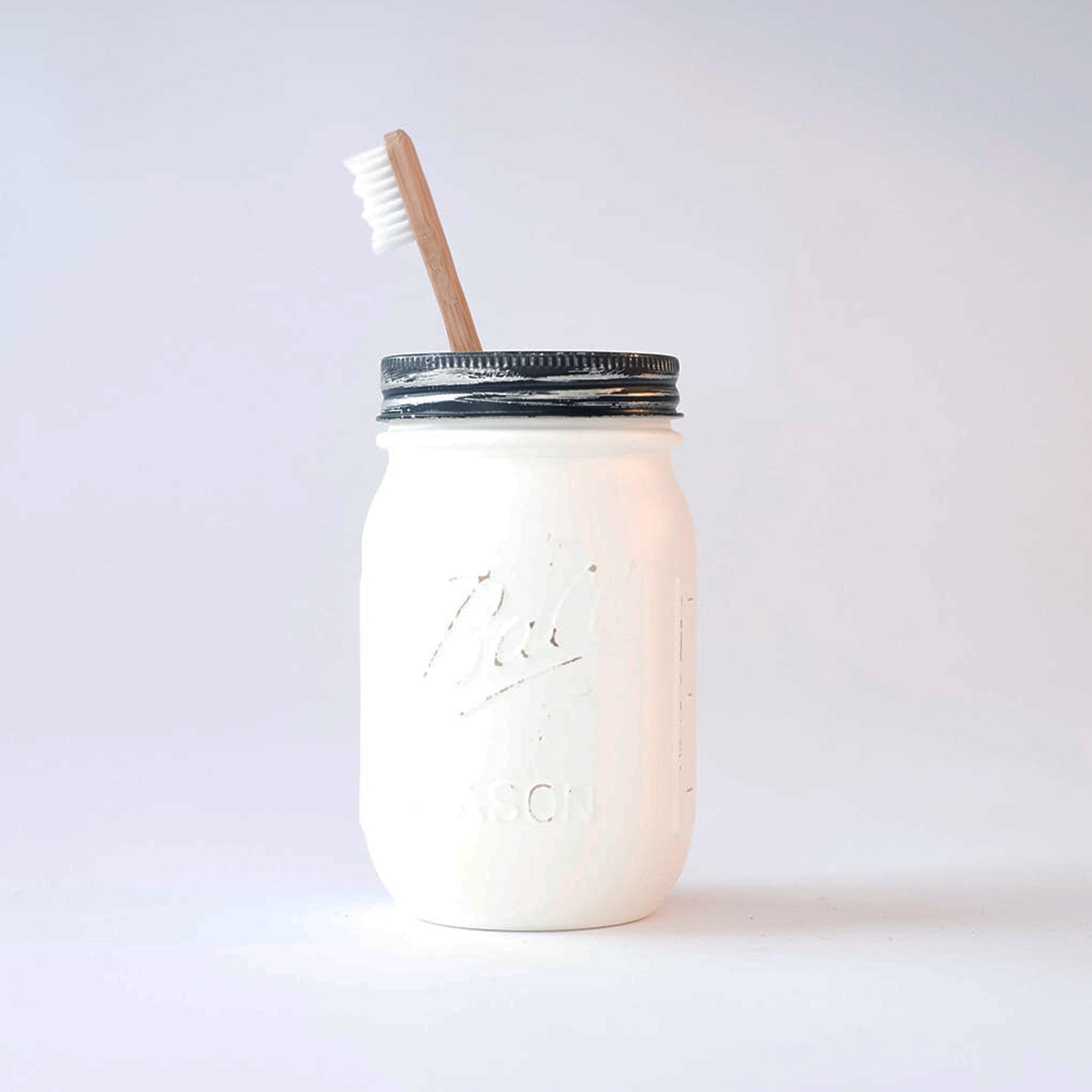 White mason jar with a silver lid and wood toothbrush on a white background.