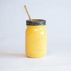 Yellow mason jar with a black lid and wooden toothbrush on a light gray background.